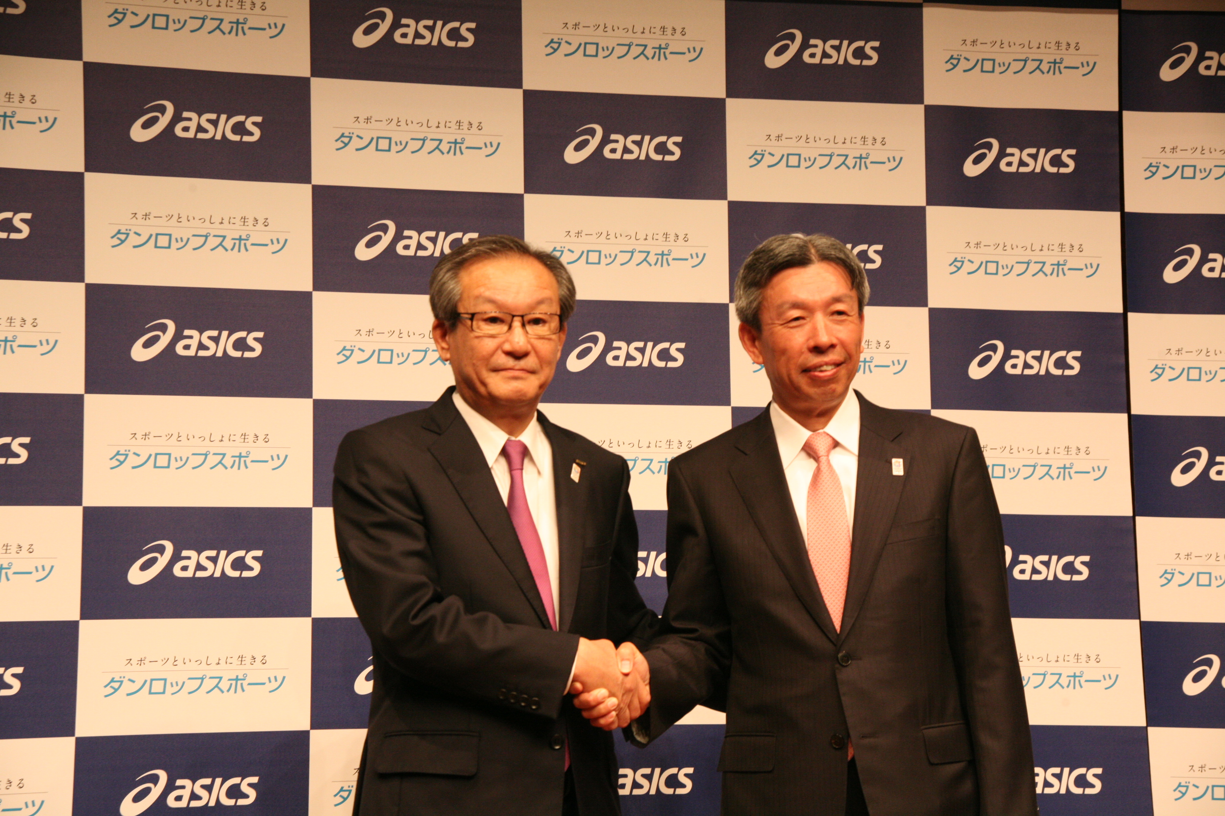 会見で握手するアシックスの尾山基社長（左）とダンロップスポーツ野尻恭社長
