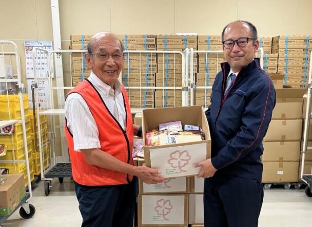 セカンドハーベスト名古屋 前川理事長(左)に食品などを手渡す同社総務部長の佐藤真臣氏